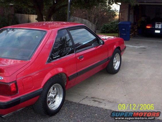 Red 1990 Ford Mustang parked in a driveway. Another car is visible in the garage behind it