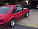 1990 Ford Mustang - A red 1990 Ford Mustang is parked outside a garage, with another vehicle visible inside.