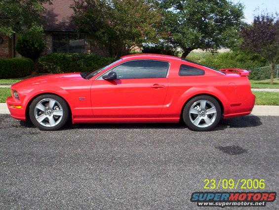 Red Ford Mustang coupe parked on asphalt, side view. Visible GT badge on fender