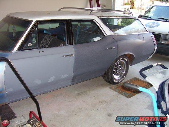 Station wagon with primer on the rear half, white roof, and chrome wheels