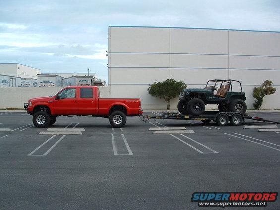 Green Jeep Wrangler on trailer towed by red Ford F-250