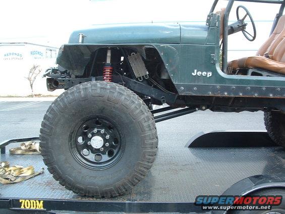 Green Jeep with large tires on a trailer, front fender removed, showing suspension