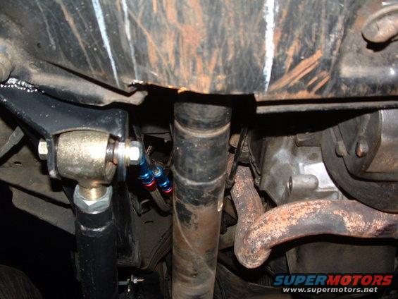 Underbody view of suspension linkage and exhaust pipe with blue and red fluid lines