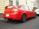 2005 Dodge SRT-4 - A red 2005 Dodge SRT-4 is parked outside a building, showing its distinctive rear spoiler and dual exhaust pipes.