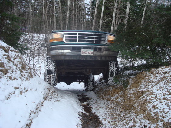 Green Ford truck with large tires driving through a snowy ditch