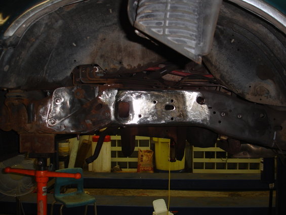 Underside view of a vehicle frame being repaired, showing rust and new welds