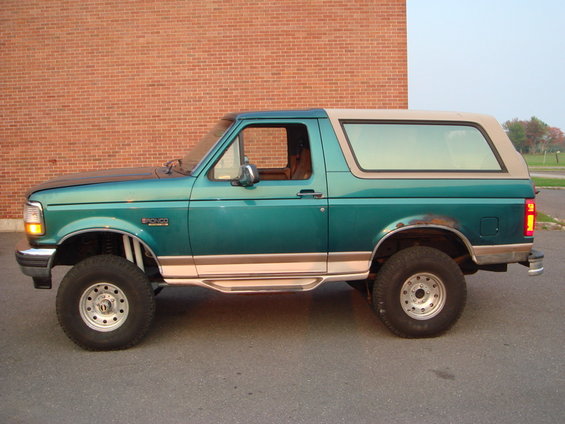 Green 1996 Ford Bronco with tan top, lifted suspension, and chrome side steps parked on asphalt