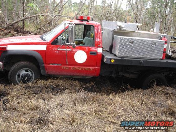 Red fire truck with "FIRE DEPARTMENT" on the door is stuck in muddy terrain with dry grass