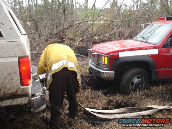 White SUV rear bumper and red truck front grille with a firefighter between them