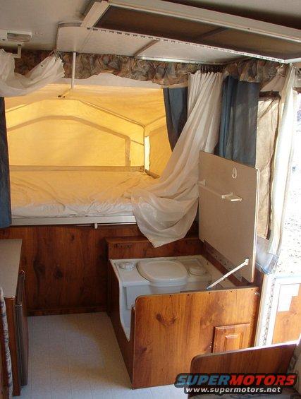 interior of pop-up camper with bed, toilet, and wood paneling