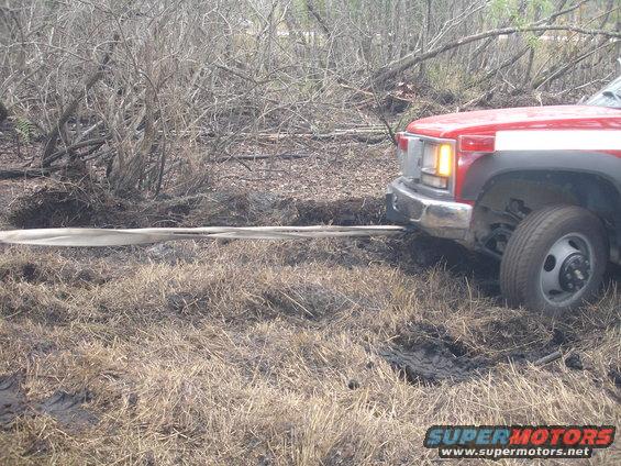 Red truck front view, pulling a strap from muddy terrain