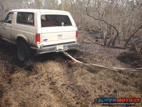1989 Ford Bronco stuck in mud with a tow strap attached to the rear bumper