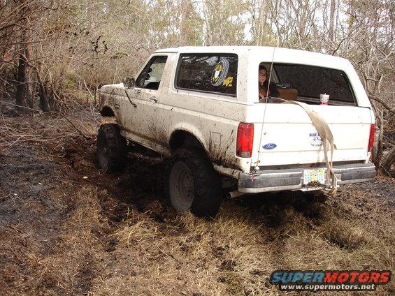 Mud-covered white Ford Bronco with lifted suspension driving off-road