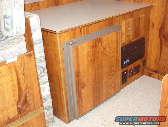Camper interior with wood paneling, a folded cushion, and a refrigerator
