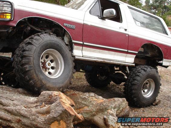 Maroon and white 1989 Ford Bronco with large off-road tires navigating logs