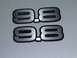 1990 Ford Mustang - Two "9.8" emblems are shown against a textured gray background.