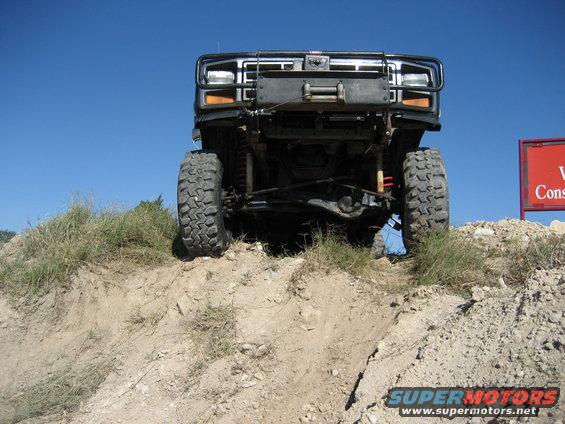 Front view of a lifted truck with large tires climbing a dirt hill