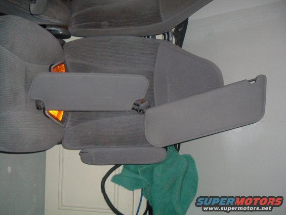 Car interior with gray fabric seats and folded-down sun visors. Orange interior light visible