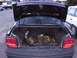 2003 Ford Ranger - The open trunk of a black sedan reveals camouflage bags and a black case, with other vehicles visible in the background.