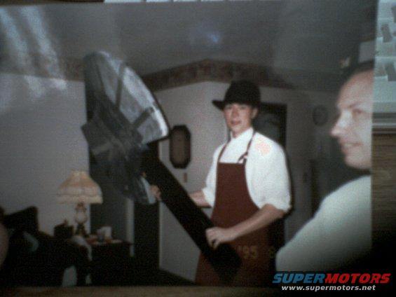 Person in hat and apron holding a large, dark object indoors