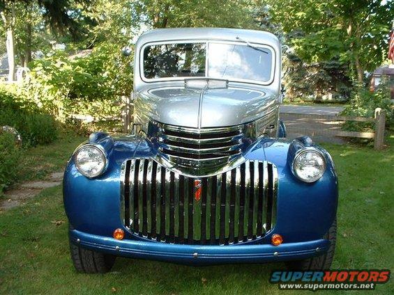 Front view of a blue and silver pickup truck with a large chrome grille. Looks like a 1940s model