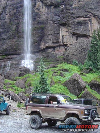 Brown Ford Bronco II with off-road tires and roof rack parked near a waterfall