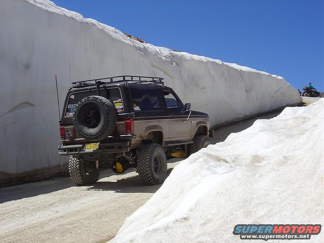 1986 Ford Bronco II with spare tire on back, driving on dirt road next to snowbank