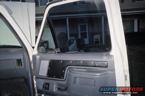Interior door panel and dashboard of a white truck. A house is visible through the window
