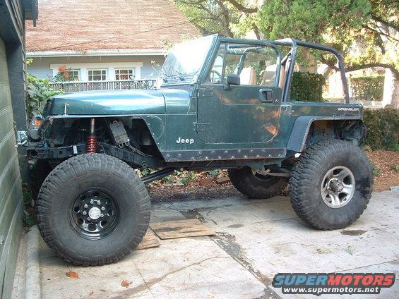 Green Jeep Wrangler with off-road tires, side view. "Jeep" and "Wrangler" visible