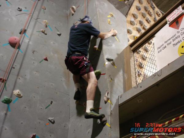 Indoor climbing wall with a person ascending, safety sign visible
