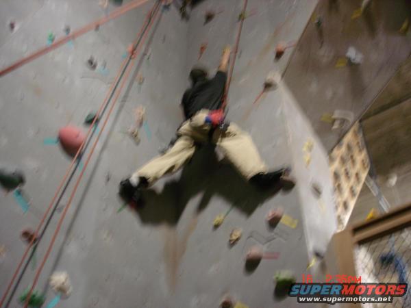 Person climbing an indoor rock wall with ropes and holds
