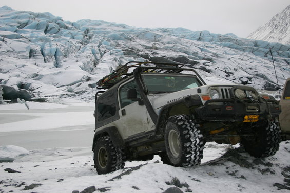 White 2003 Jeep TJ Rubicon with roof rack on snowy terrain near a glacier