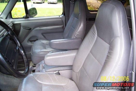 Gray leather bucket seats and center console in a vehicle. Steering wheel visible on left. Two other vehicles seen through the window