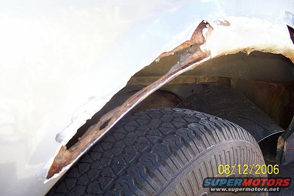 close-up of heavily rusted metal in a vehicle's wheel well, showing a tire and part of the undercarriage