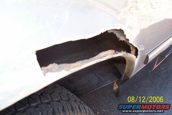 White vehicle's rear wheel well with extensive rust damage and a hole exposing the interior