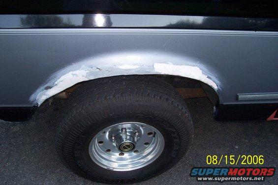 Vehicle rear wheel well with body filler and primer, showing rust damage