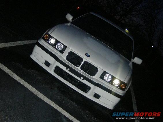 White BMW E36 coupe front view at night. Halo headlights are on