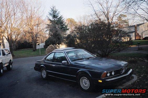 Dark blue BMW coupe parked on street, white SUV in background