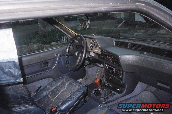 Dark blue leather interior of a BMW E24 6 Series coupe, showing cracked seats, dashboard, and steering wheel