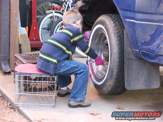 Blue car side view, child in jeans and striped sweater with pink gloves works on wheel