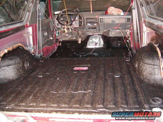 Interior of a red SUV with exposed wiring and a dark, textured floor. The dashboard and steering wheel are visible