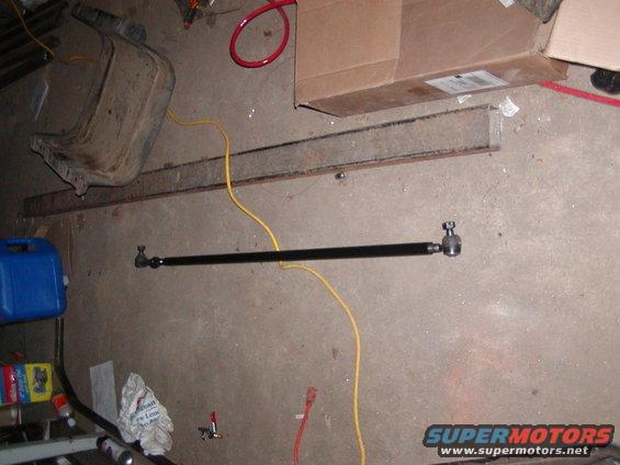 Black steering linkage rod with tie rod ends on a concrete floor
