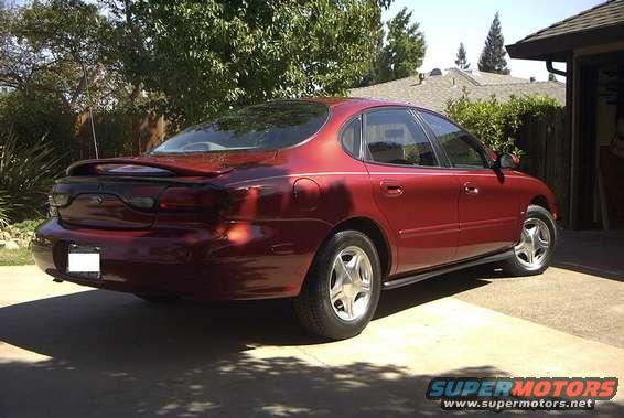 Red sedan parked in driveway, rear quarter view. It has a spoiler and aftermarket wheels