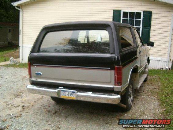 Rear view of a 1986 Ford Bronco with a black top and silver lower body. License plate reads GKL-1999