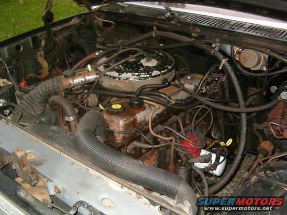 Engine bay with hoses, wires, and engine components visible. Water stains on engine parts