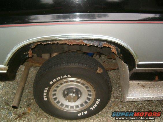 1986 Ford Bronco rear wheel well with extensive rust and a steel radial tire