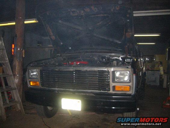 Black SUV front view, hood open, showing engine. License plate illuminated
