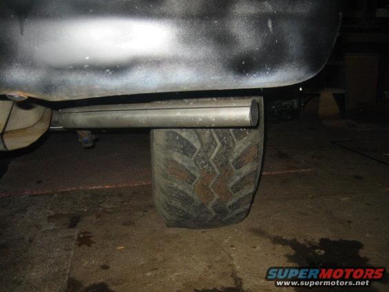 Close-up of a large tire and exhaust pipe under a vehicle