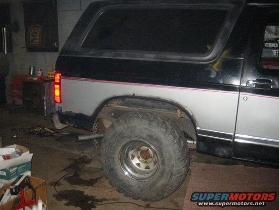 Rear quarter panel of a black and silver Ford Bronco, parked indoors with the rear brake light illuminated