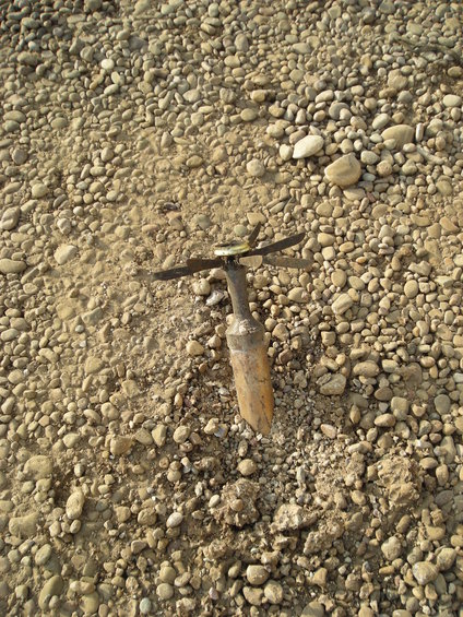 Wooden stake with metal blades stuck in gravel
